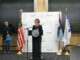 Director Rachel Sayre speaks at the podium at the swearing in ceremony held on Oct. 21 at the City’s Emergency Operations and Training Facility. From left to right, Office of Community Safety Commissioner Todd Barnette, City Clerk Casey Carl, Director Sayre, and Mayor Jacob Frey (SOURCE: Minneapolis Office of Community Safety)